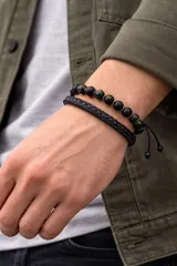 Set de dos pulseras para hombre, una compuesta por cuentas esféricas negras y la otra de cadena metálica trenzada en color gris oscuro.