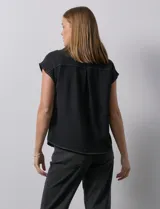 Blusa negra con cuello con solapa y escote en V, con bolsillos delanteros y pespuntes blancos.