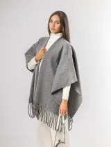 Ruana gris de tejido de punto con flecos en el ruedo.