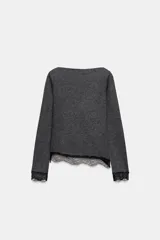 Top de manga larga en tejido suave color gris, con cuello redondo y bajo asimétrico decorado con encaje negro a tono. Presenta detalles de encaje negro en los puños.