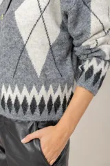 Cardigan de punto con diseño de rombos en tonos gris, blanco y negro. Presenta cuello redondo, cierre frontal con botones dorados y mangas largas.