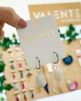 Aros colgantes con aro de acero plateado y dije cilíndrico de resina color crema con vetas marrones.