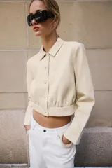 Camisa crop de manga larga con cuello solapa y cierre frontal de botones, confeccionada en tejido sintético con efecto piel color beige.