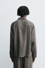 Camisa de corte relajado confeccionada en tejido fluido con mezcla de modal, presenta un diseño de rayas verticales con textura efecto arrugado, cuello solapa, cierre frontal de botones y manga larga con puños abotonados.