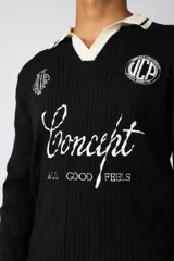 Sweater de punto acanalado en color negro, con cuello polo en contraste color crema. Presenta detalles bordados en el pecho y estampado tipográfico central con la frase 'Concept ALL GOOD FEELS'.
