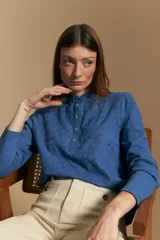 Blusa de algodón color azul con textura bordada, cuello con volado y cierre frontal con botones. Presenta mangas largas y un calce relajado.