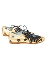 Zapatos tipo blucher artesanales de napa dorada con estampado de estrellas negras. Presentan un adorno de flecos de napa negra en el empeine, cierre con cordones y suela de cuero.