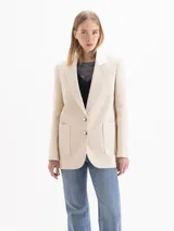 Blazer de tweed color beige, de corte recto y largo medio, con solapa clásica en contraste color blanco, dos bolsillos frontales con parche y cierre de dos botones plateados.