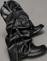Botas altas de cuero sintético negro con diseño slouchy, suela plana y detalles de tiras colgantes con argollas metálicas.