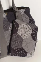 Bolso tipo tote amplio, confeccionado en patchwork de hexágonos con diferentes estampados en tonos azul marino y blanco/gris. Presenta asas y base en tela lisa gris. El cuerpo del bolso tiene un efecto acolchado.