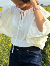 Blusa blanca de manga larga abullonada con volados y cuello redondo con cordones para atar.