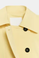 Chaqueta corta confeccionada en mezcla de algodón color amarillo claro, con cuello de solapa, manga larga, bolsillos delanteros y cierre frontal con botones visibles en los extremos.