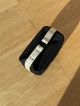 Neceser de neopreno color borgoña, con cierre superior y forro interior. Tiene un asa de mano con una franja azul y blanca.