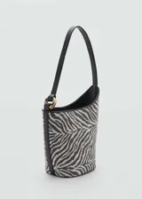 Bolso tipo bucket con estampado de cebra en tonos grises y negros. Tiene asa corta, cierre de botón magnético, detalle metálico dorado y forro interior.
