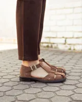 Sandalias de cuero gamuzado color marrón, tipo romanas, con tiras entrelazadas, talón cerrado y tira ajustable con hebilla metálica en el tobillo.
