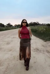 Pollera midi de cuero marrón con diseño asimétrico y flecos largos que aportan movimiento y textura.