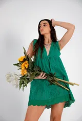 Vestido corto color fucsia, con escote en V profundo y mangas cortas tipo volado. Presenta un diseño con textura de bordado inglés o perforado y un corte imperio con frunce que da volumen a la falda.