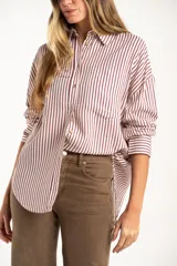 Camisa de corte oversize con estampado de rayas verticales, cuello clásico, cierre frontal con botones y bolsillo en el pecho. Presenta mangas largas con puños abotonados y un diseño fluido.