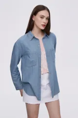 Sobrecamisa celeste de denim con cuello camisero, cierre frontal con botones a presión, dos bolsillos con solapa en el pecho y mangas largas con puños abotonados.