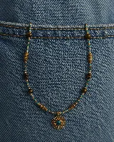 Collar de cuentas pequeñas en tonos turquesa, dorado y transparente, intercaladas con cuentas de madera y piedras marrones. Presenta un dije central en forma de sol dorado con una piedra turquesa en el centro.