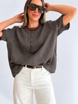 Blusa de lino color beige con cuello redondo, mangas cortas y cierre frontal parcial con botones oscuros.