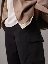 Shorts cargo negros de corte recto y talle medio, confeccionados en sarga de algodón elástico. Cuentan con cierre de botón y cremallera, cintura elástica en los laterales, bolsillos laterales, bolsillos traseros ribeteados y bolsillos cargo. Incluyen etiqueta con el logo de Calvin Klein sobre el bolsillo trasero.