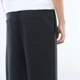 Pantalón de corte ancho y estilo jogging, confeccionado en tejido liso de color negro, con cintura elástica y diseño minimalista.