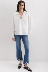 Camisa blanca de algodón, de corte holgado, con cuello clásico, mangas largas con puños anchos y un bolsillo de parche en el lateral.