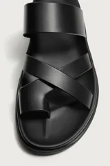 Sandalia de cuero sintético color negro con diseño de tiras cruzadas y sujeción para el dedo. Cuenta con plantilla anatómica y suela plana a tono.