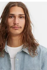 Camisa de manga corta con diseño de rayas verticales tipo railroad, cuello clásico y cierre frontal con botones. Presenta dos bolsillos en el pecho con solapa y un corte relajado.