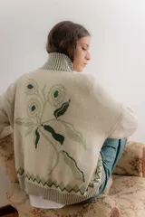 Saco tejido tipo jacquard color bordó con diseño floral en la espalda, cuello alto y cierre frontal de aluminio. Presenta detalles en azul y blanco en el cuello, puños y ruedo, con un patrón geométrico de rombos en la parte inferior.