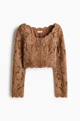 Cropped top de manga larga color marrón en punto estilo crochet con diseño en hilo de chenilla y ribetes festoneados. Cuenta con escote en U y botones forrados al frente, con forro de punto.