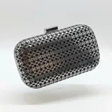 Clutch rígido de metal color peltre, con diseño calado de patrón geométrico de anillos entrelazados y cierre superior de broche metálico.