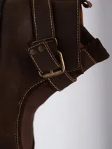 Bota corta tipo borcego de cuero negro con textura granulada, suela track dentada y tira decorativa con hebilla metálica en el tobillo.