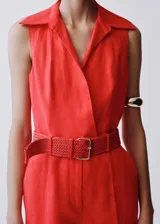 Mono camisero color rojo coral, sin mangas, confeccionado en lino. Presenta cuello camisero, cierre frontal cruzado, cinturón trenzado desmontable y corte palazzo.