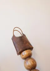 Bolso tipo matera de cuero con textura de reptil, color tostado, con manijas trenzadas y detalles de costura artesanal en los bordes.