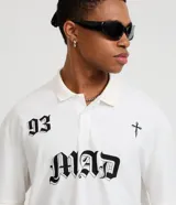Remera de corte boxy confeccionada en algodón, con cuello polo y cierre frontal de botones. Presenta un diseño estampado en el frente con el número 93, una cruz y la palabra MAD en tipografía gótica.