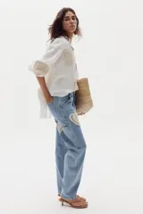 Pantalón estilo cargo confeccionado en denim celeste, de corte recto y holgado. Presenta apliques decorativos circulares de crochet en tonos beige en los laterales y bolsillos utilitarios.