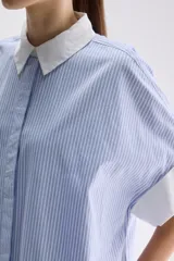Vestido camisero midi de calce relajado a cuadros en tonos verde y negro, confeccionado en algodón liviano. Presenta cuello clásico en contraste de color blanco, cartera frontal oculta con botones y mangas cortas con vuelta.