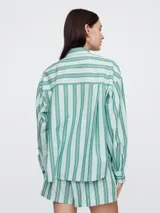 Camisa de corte oversize confeccionada en popelina, con diseño de rayas verticales en tonos verde y blanco. Presenta cuello clásico, cierre frontal con botones y bolsillo en el pecho.