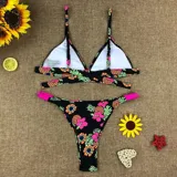 Bikini de diseño tropical con estampado de hibiscos y piñas sobre fondo negro. El top es de estilo triángulo con tiras cruzadas en el torso y la bombacha es de corte tanga con tiras laterales en color coral.