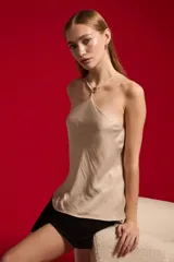 Top de poliéster color beige, con diseño holgado, cuello halter y detalle de aplicación metálica en el escote.