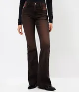 Pantalón de jean corte flare con lavado sobretinta en tono marrón oscuro. Presenta cintura media con trabillas, cierre frontal con cremallera y botón, cinco bolsillos funcionales y ruedo deshilachado.