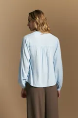 Camisa de manga larga color blanco, con cuello mao y escote en V. Presenta frunces en el canesú, cierre frontal con botones y mangas amplias con puños abotonados.