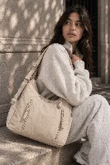 Cartera hobo gris de tela suave y liviana, con bolsillos frontales con cierre y tiradores trenzados, correa ajustable y compartimento principal con cierre.