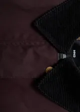 Parka color bordó, de corte recto, con cierre frontal de cremallera y botones a presión. Presenta cuello camisero de pana, bolsillos frontales de parche con solapa y mangas largas con puños ajustables. Incluye forro interior.