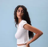 Top corto de manga corta, color blanco jaspeado, con escote en V y ribete de costura en color rojizo/marrón en el cuello y los bordes de las mangas. Presenta un pequeño bordado de corazón en el pecho.