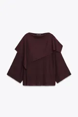 Jersey de punto color vino tinto, de corte amplio y holgado, con cuello bote y un detalle de capa asimétrica superpuesta en la parte superior delantera. Mangas anchas tipo murciélago.