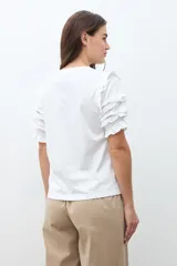 Remera de algodón color terracota con cuello redondo y mangas cortas con detalle de volados escalonados y costuras decorativas.