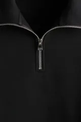 Buzo negro de corte holgado, confeccionado en tejido pesado de mezcla de algodón con interior cepillado. Cuenta con hombros caídos, cuello elevado con medio cierre metálico, y puños y bajo en punto acanalado.